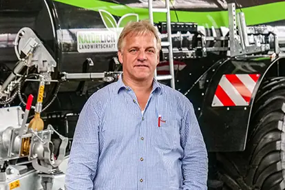 Ein Mann steht vor einem landwirtschaftlichen Fahrzeug, das auf der Seite mit "NATÜRLICH LANDWIRTSCHAFT" beschriftet ist, Sponsoren.
