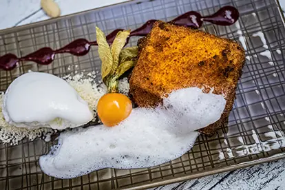 Frittierte Milch mit Mandelschaum, Sauerrahmmeis, einer Beerenreduktion und essbaren Blättern auf einem dekorativen Teller.
