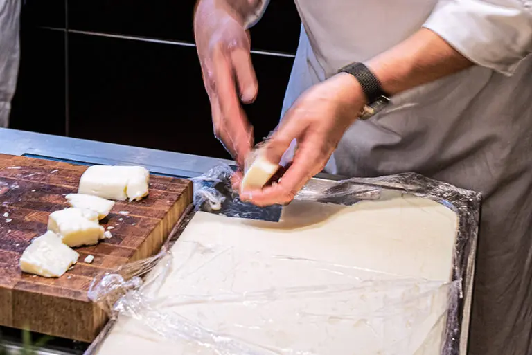 Ein Koch formt Käse während des Milchworkshops auf einer Holzplatte.