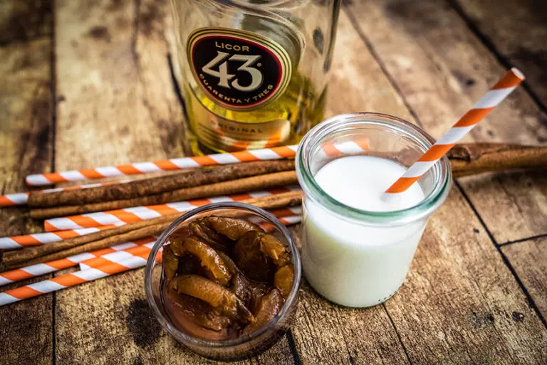 Koch-Workshop Milchworkshop mit Licor 43, Zimtstangen, Milch und Trockenfrüchten auf einer Holzoberfläche.