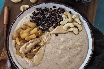 Apfel-Zimt-Grießbrei mit Äpfeln, Kakaonibs, Cashewkernen und Erdnussbutter in einer Schüssel angerichtet.