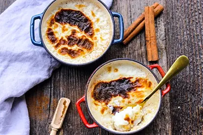 Türkischer Milchreis in zwei Schalen mit goldbraunem Belag und Zimtstangen auf einem rustikalen Holzuntergrund.