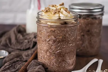 Lebkuchen Overnight Oats in einem Glas, garniert mit Bananenscheiben und Keksen, auf einem rustikalen Tisch.