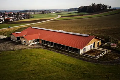 Luftaufnahme eines modernen Bauernhofs mit rotem Dach, umgeben von Feldern und einer ländlichen Umgebung.
