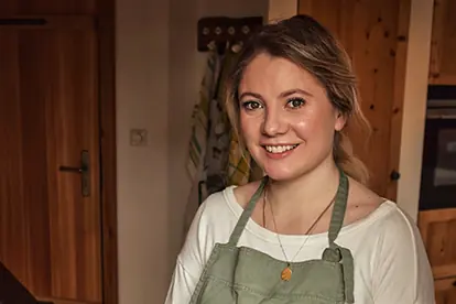 Junge Frau in einer gemütlichen Küche, die ein freundliches Lächeln zeigt und eine Schürze trägt.