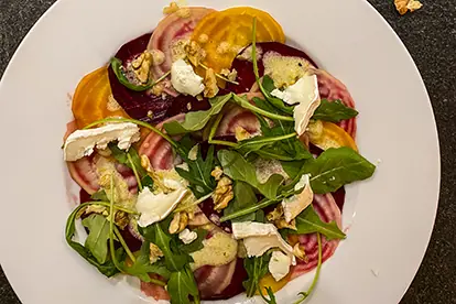 Bunte Bete Carpaccio mit Rucola, Ziegenkäse und Walnüssen auf einem weißen Teller.