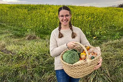 Eine Frau mit einem Korb voller frischer Zutaten steht vor einem Feld, ideal für die Zubereitung von Bunte Bete Carpaccio.