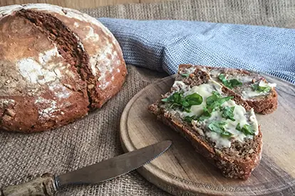 Roggenvollkornbrot mit Sonnenblumenkernen, serviert mit Butter und frischen Kräutern auf einem Holzbrett.