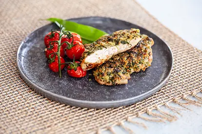 Krustiger Schnitzel mit Karamellzwetschgen und gerösteten Tomaten auf einem grauen Teller.
