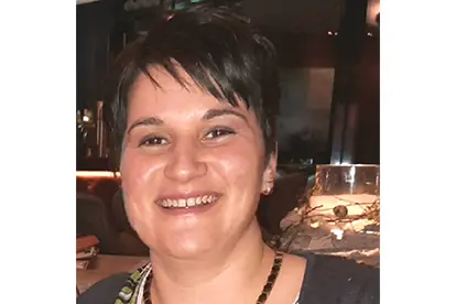 Eine lächelnde Frau mit kurzen, dunklen Haaren in einem modernen Restaurantumfeld, die Freude am Essen ausstrahlt.