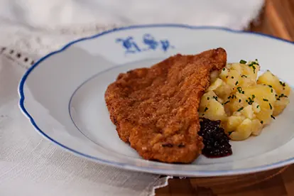 Schnitzel mit Karamellzwetschgen und Kartoffelsalat auf einem eleganten Teller serviert.