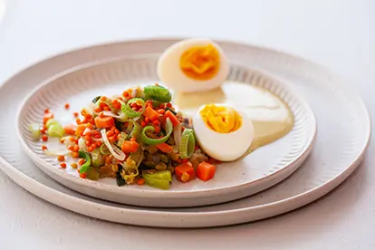 Bunter Dinkelsalat mit Gemüse, serviert mit einem weichgekochten Ei und einer cremigen Sauce auf einem eleganten Teller.