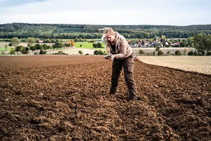 Eine Person untersucht den Boden auf einem Acker, um die Praktiken des Carbon Farmings zu demonstrieren.
