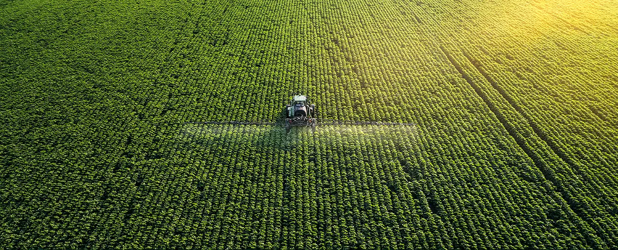 Traktor sprüht Dünger über ein grünes Feld zur teilflächenspezifischen Düngung in der Landwirtschaft.