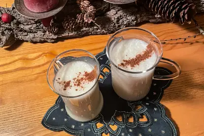 Zwei Gläser Wintermilch mit Zimt, dekoriert auf einem Tisch mit Adventsdeko und Naturmaterialien.