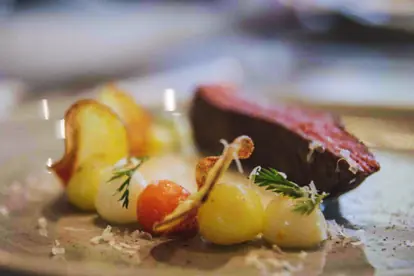Rinderlende mit Blauschimmelkäse-Soße, buntem Gemüse und knusprigen Kartoffelchips auf einem eleganten Teller angerichtet.