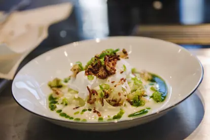 Blumenkohlpüree mit Spitzkohlsalat, pochiertem Ei und Petersilienöl in einer eleganten Schale angerichtet.