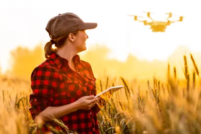 Eine Landwirtin beobachtet einen Drohnenflug über einem Weizenfeld, das für smart farming-Technologien genutzt wird.