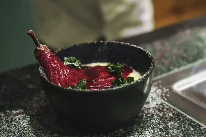 Leichtes Panna Cotta mit einer in Rotwein pochierten Birne und frischen Minzblättern in einer dunklen Schüssel.