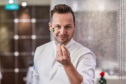 Ein Koch präsentiert stolz eine dekorative Zutat für das Panna Cotta mit pochierter Birne in einem eleganten Restaurant.