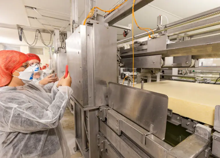 Zwei Mitarbeiterinnen in Schutzkleidung arbeiten an einer automatisierten Produktionsmaschine in einer Lebensmittelverarbeitung.