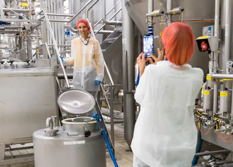 Zwei Personen in Schutzkleidung fotografieren in einer modernen Produktionsumgebung mit Maschinen und Tanks.