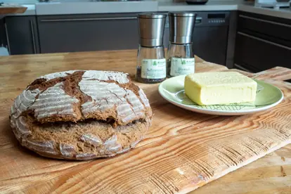 Roggenbrot und Butter auf einem Holzbrett, mit Salzstreuern im Hintergrund, bereit zum Servieren.