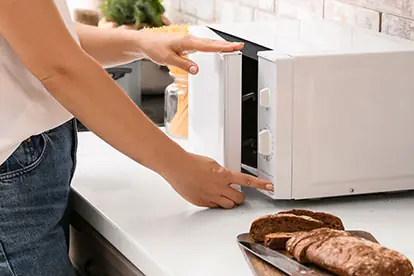 Eine Person nutzt eine Mikrowelle, um altes Brot zu verwerten und es wieder aufzuwärmen.