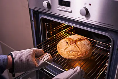Ein Hand mit Ofenhandschuhen entnimmt ein frisch gebackenes Brot aus dem Ofen, um altes Brot zu verwerten.