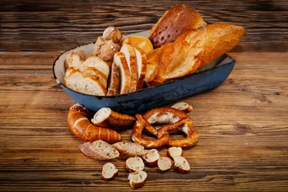 Verschiedene Brotsorten und Brezeln in einer blauen Schüssel auf einer Holzoberfläche arrangiert.