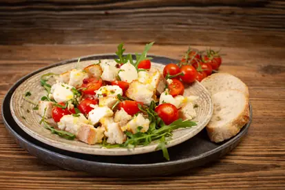 Knödelcarpaccio mit Kirschtomaten, Rucola und frischem Brot auf rustikalem Teller.