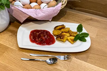 Kaiserschmarrn mit Rhabarber-Kompott auf einem Teller, dekoriert mit frischer Minze und umgeben von Eiern in einem Korb.