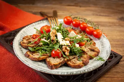 Knödelcarpaccio mit Rucola, Kirschtomaten und Walnüssen auf einem rustikalen Teller.