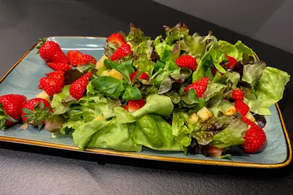 Bunter gemischter Salat mit frischen Erdbeeren und Käse auf einem türkisfarbenen Teller.