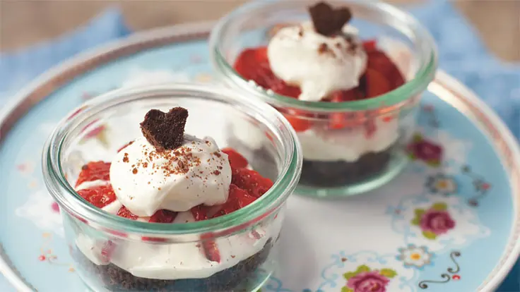Erdbeer-Weißbier-Tiramisu in Gläsern mit Erdbeeren, Sahne und Schokoladenherz auf einem dekorativen Teller.