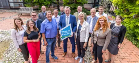 Der neue Vorstand von "Unsere Bayerischen Bauern" versammelt sich im Freien, lächelnd und mit einem Schild in der Mitte.