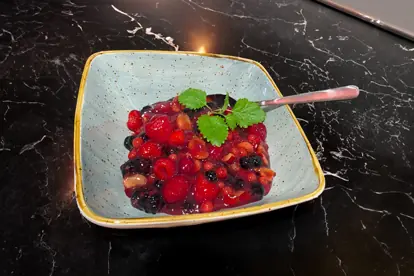 Fruchtsalat mit Himbeeren, Erdbeeren und Heidelbeeren in einer blauen Schale, garniert mit frischen Minzblättern.