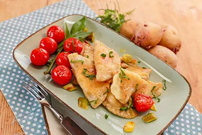 Gefüllte Kartoffelnudeln mit Kirschtomaten und frischen Kräutern auf einem Teller, umgeben von rohen Kartoffeln.