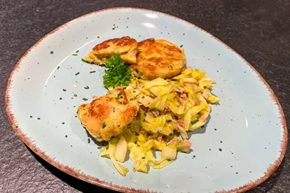 Kaspressknödel auf einem Teller mit Spitzkohlgemüse und frischem Schnittlauch dekoriert.
