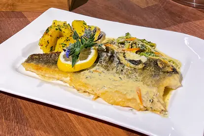 Gebratenes Fischfilet mit Senfsoße, serviert auf Gemüsestreifen und Beilagen aus Kartoffeln und Zitrone.