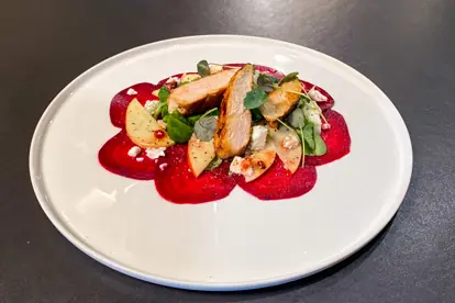 Hähnchenbrust auf Feldsalat mit Roter Bete, Apfelscheiben und Schafskäse auf einem weißen Teller angerichtet.