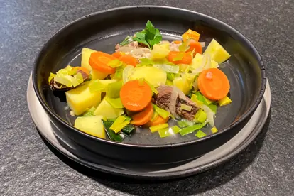 Ein bunter Pichelsteiner Eintopf mit Kartoffeln, Karotten, Lauch und Fleisch in einer schwarzen Schüssel.
