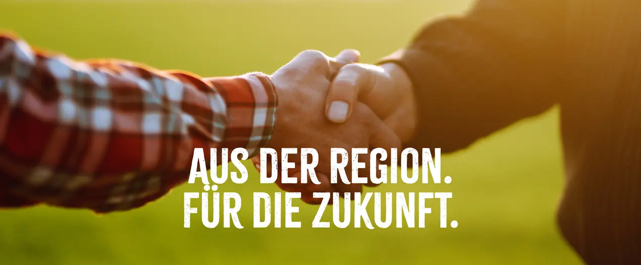 Händedruck vor einer grünen Wiese symbolisiert Zusammenarbeit für die Heimat der Vielfalt und eine nachhaltige Zukunft.