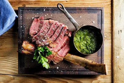 Saftiges Steak auf Holzbrett mit frischem Chimichurri und Petersilie, serviert in einer Metallkelle.