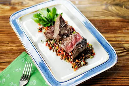 Gegrilltes Hüftsteak auf einem Bett aus buntem Gemüsesalat und Linsen, garniert mit frischen Kräutern.