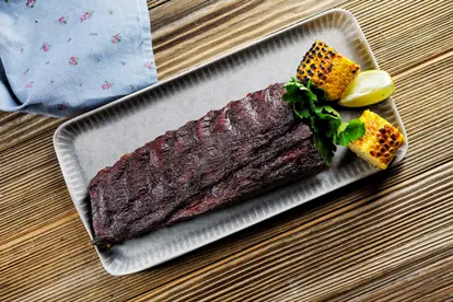 Gegrillte Rinderlende serviert mit gegrilltem Mais und Limette auf einem rechteckigen Teller.