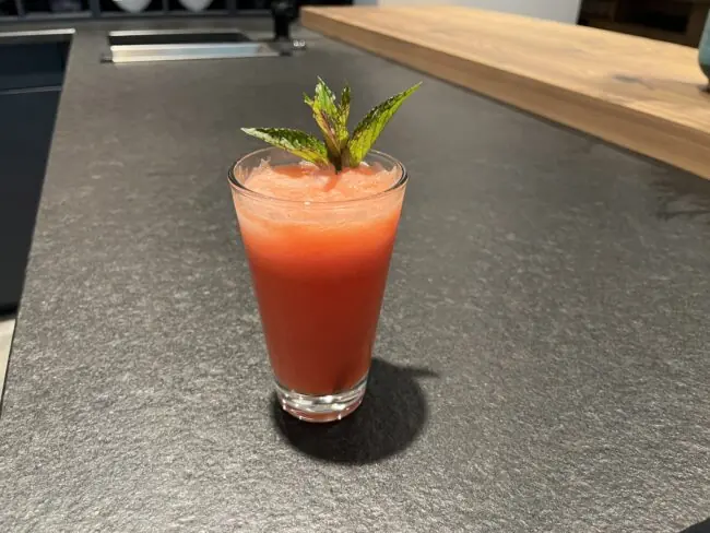 Erfrischender Wassermelonen-Cocktail mit Minze in einem Glas auf einer dunklen Arbeitsfläche.