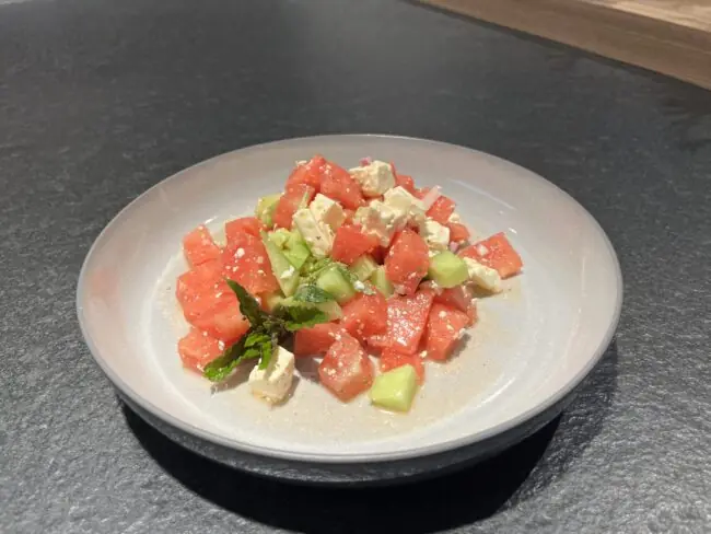 Frischer Salat aus Wassermelone, Gurke und Feta, garniert mit Minze, serviert auf einem flachen Teller.