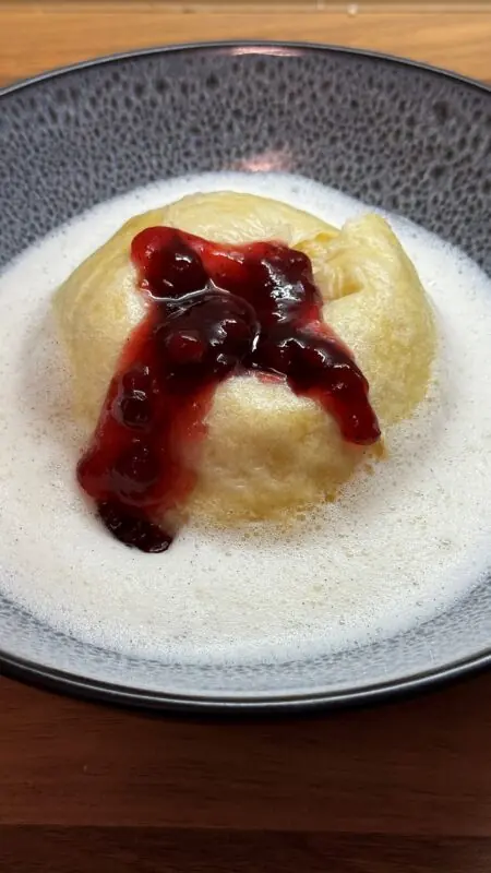 Dampfnudeln mit Vanillesoße, bedeckt mit roter Fruchtsoße, serviert in einer dekorativen Schüssel.