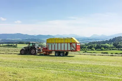 Ein Traktor mit Anhänger erntet auf einem grünen Feld in einer malerischen Landschaft, ein Beispiel für Agrartechnik.